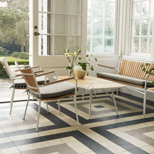 En stilfuld solstue med store vinduer, med et geometrisk sort og hvidt klinkegulv, en moderne beige sofa, to matchende stole fra TomorrowsDesign og et rundt træbord med en vase med gule blomster.