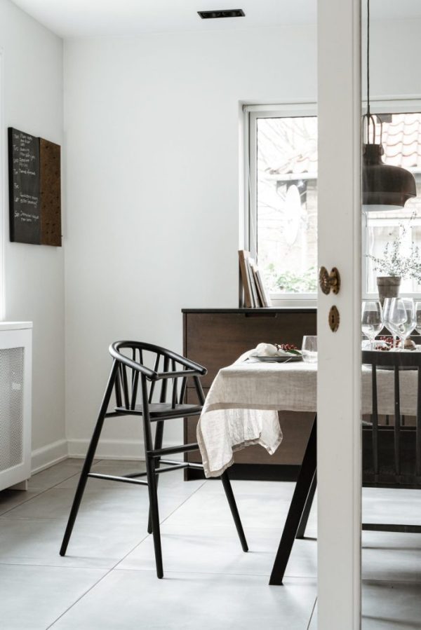En minimalistisk spisestue set gennem en døråbning med TomorrowsDesign-møbler såsom et træbord med en hvid klud og en enkelt sort stol. Neutrale vægge og klinkegulve, med naturligt lys ind gennem et vindue.