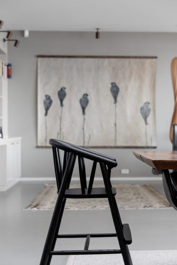 En sort træskammel i fokus i forgrunden, med en sløret baggrund med en moderne spisestue med minimalistisk kunst, der forestiller fire fugle på en væg over et designmøblertæppe.