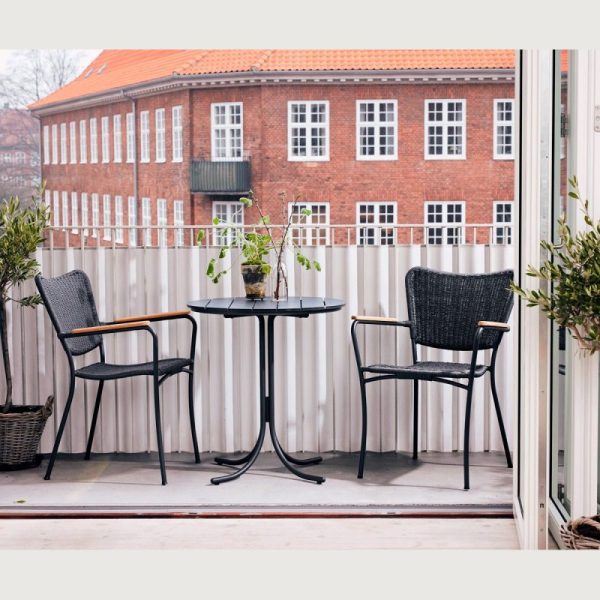 En hyggelig altanopstilling med to kurvestole og et lille rundt bord, med potteplanter og udsigt over en klassisk murstensbygning ud over et hvidt hegn, er indbegrebet af TomorrowsDesigns æstetik.