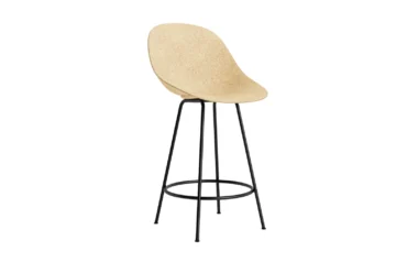 En moderne NORMANN COPENHAGEN - Mat Barstoll 65 med et lys beige, buet sæde på et slankt sort metalstel med tynde, aflange ben og en cirkulær fodstøtte. baggrunden er almindelig hvid.