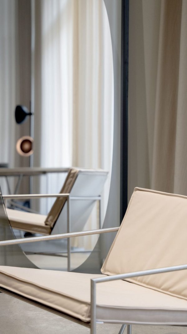 Moderne stuescene med et TomorrowsDesign-glasbord og slanke stole med metalramme med lyse beige hynder. Et rent hvidt gardin skjuler delvist et vindue i baggrunden.
