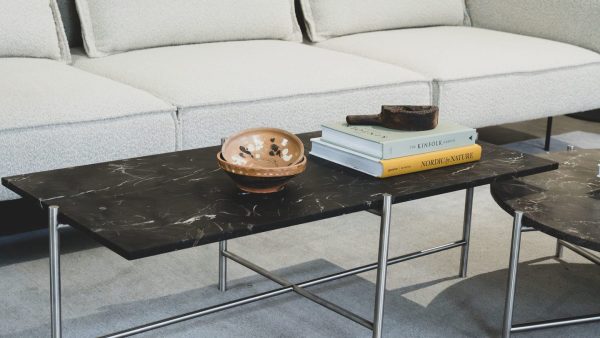 En moderne stue med en hvid sofa og to sorte marmorborde med bøger og en dekorativ kobberskål fremviser udsøgte designelementer.