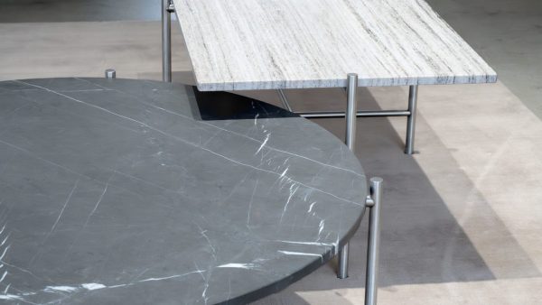 Et nærbillede af to moderne borde, det ene cirkulært med mørk marmorplade og det andet rektangulært med en let struktureret overflade, understøttet af slanke metalben fra TomorrowsDesign.