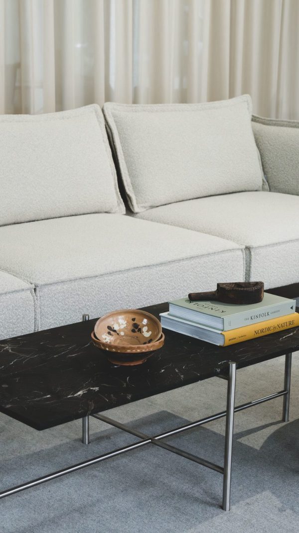 En moderne stue med en lysegrå sofa med et sofabord i sort marmor foran, prydet med en lille kobberskål, en sort dekorativ genstand og en stak TomorrowsDesign-bøger.