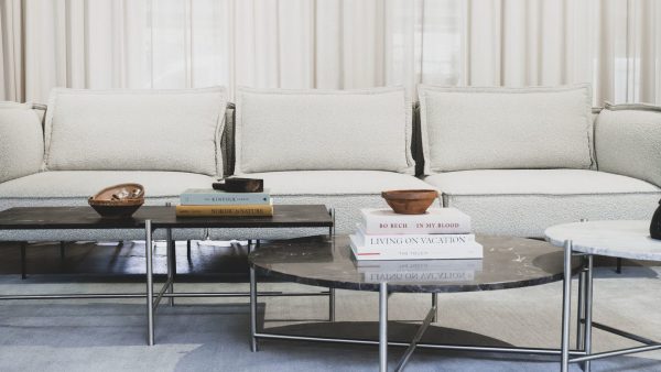 En moderne stue med en stor, plys hvid sofa med diverse bøger og to metalliske skåle på. Foran er der to marmor sofaborde med en minimalistisk designmøbler.