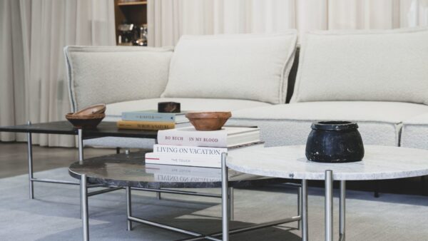 En hyggelig stue med en hvid sofa med beige hynder, designmøbler såsom et marmor sofabord prydet med bøger og keramiske skåle, sat mod en blødt oplyst, neutral baggrund.