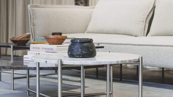 En moderne stue med et marmorsofabord med bøger og en sort gryde på, ved siden af en lys beige sofa og en træskål på en sideskammel fra TomorrowsDesign.