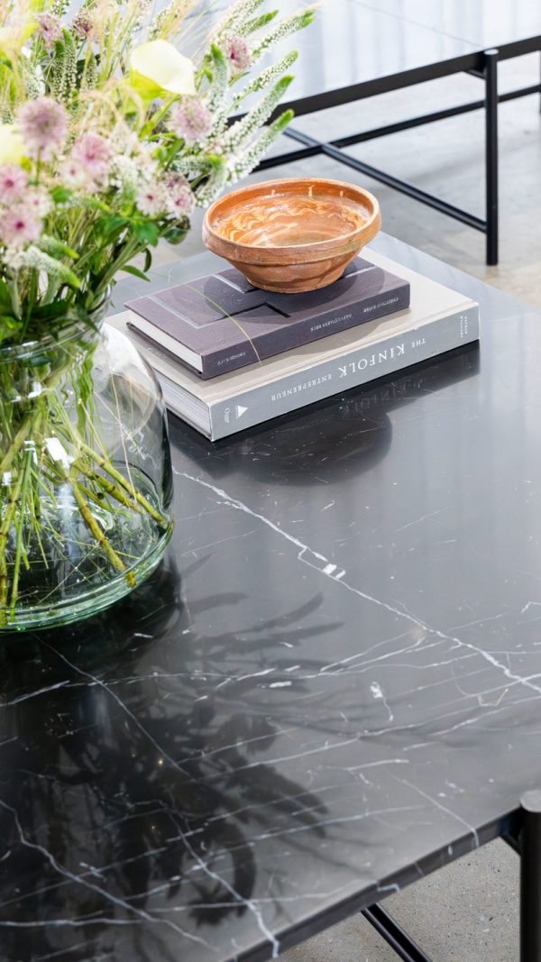 Et moderne marmorbord med en stak designbøger toppet med en rustik skål sammen med en vase fyldt med diverse blomster. Indstillingen inkluderer en enkel sort metalstol.