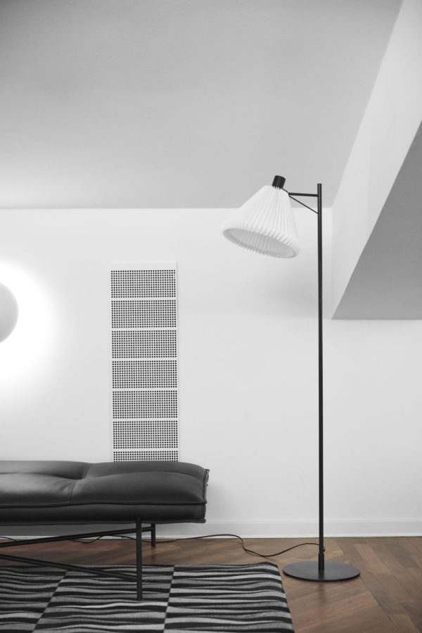 En moderne minimalistisk stue med en sort lædersofa, en høj gulvlampe med hvid skærm og et mønstret tæppe. Et dekorativt designmøbler radiatorpanel monteres på væggen i tilknytning til sofaen.