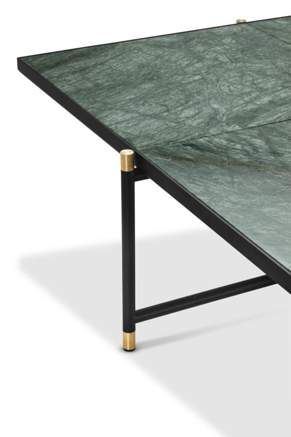 Nærbillede af et moderne designbord med en grøn marmorplade og en sort metalramme, med stilfulde guldaccenter ved leddene; isoleret på en hvid baggrund.