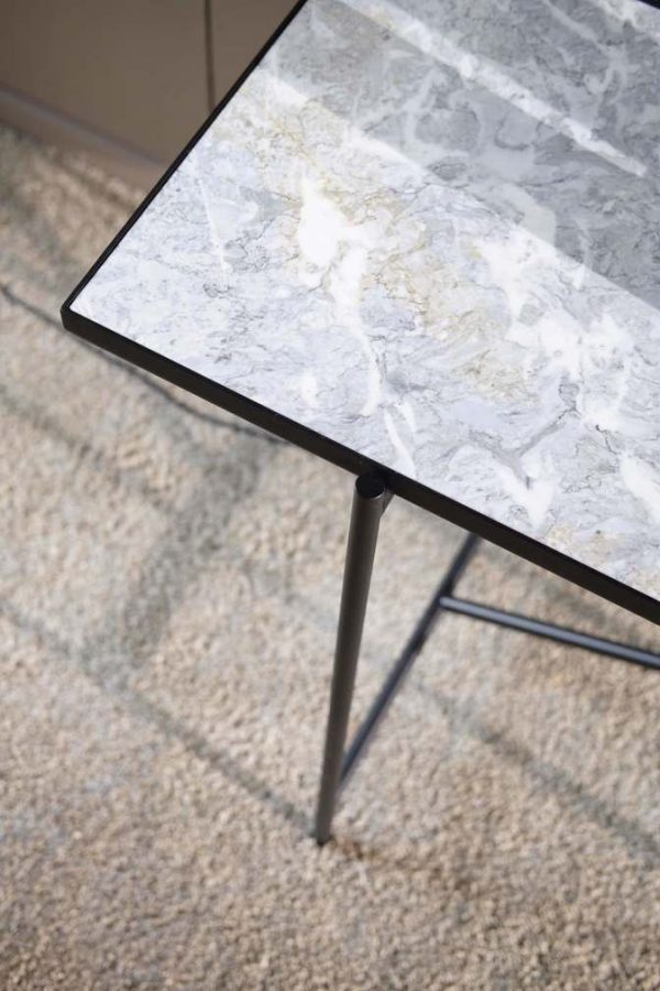 Nærbillede af et moderne bord med marmorplade og sorte metalben, sat på et tekstureret beige tæppe. Fokus er på hjørnet af bordet, der viser detaljer om møblers overflade og ramme.