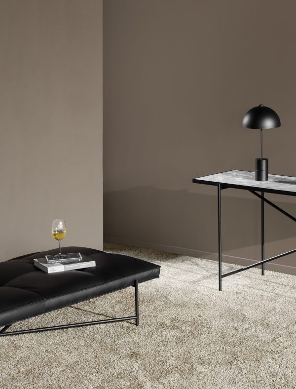 En minimalistisk stue med en lækker sort bænk, designmøbler metalbord med marmorplade og en moderne lampe på bordet. Der er et glas vin og en åben bog på bænken, alt sammen under blød belysning.