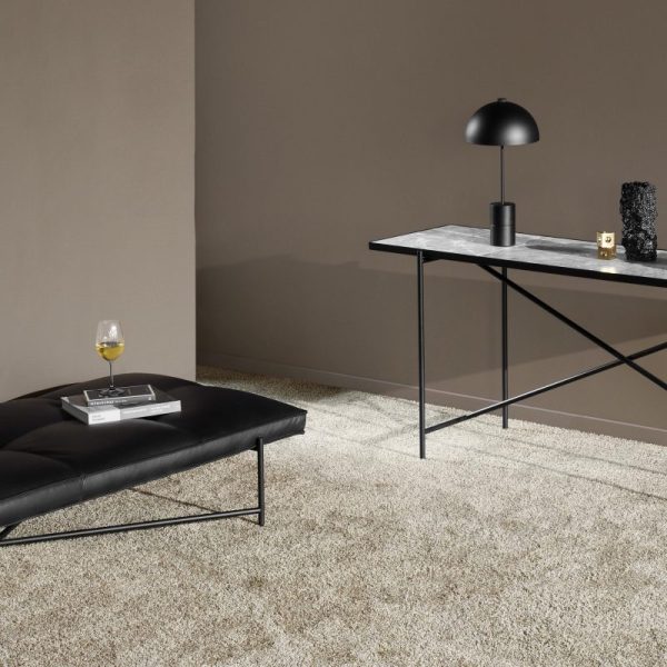 Moderne minimalistisk stuehjørne med et sort metalbord med en marmorplade fra TomorrowsDesign, en matchende lampe og tilbehør, en lav sort skammel og et glas vin på et beige gulvtæppe.