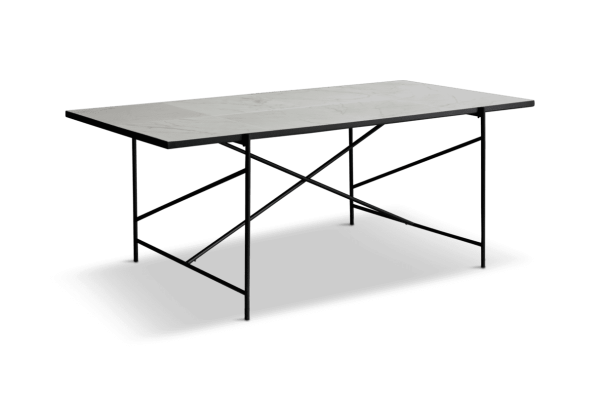 Et moderne skrivebord med hvid marmorplade og sort metalramme, sat på en sort måtte mod en grøn baggrund. Skrivebordet har et indvendigt geometrisk, x-formet bendesign.