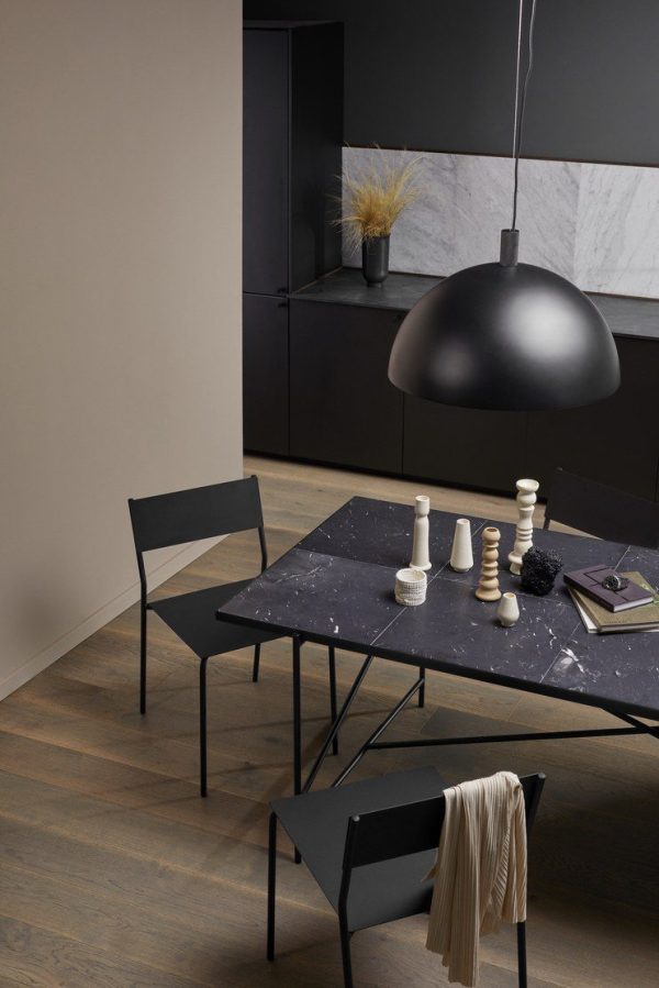 En moderne spiseplads med et sort marmorbord med to sorte stole. En stor sort pendel hænger over bordet og et mørkt skab med dekorationsgenstande står i baggrunden mod en beige væg. Disse elegante rammer viser eksklusive designmøbler, der fremhæver sofistikerede interiørvalg.