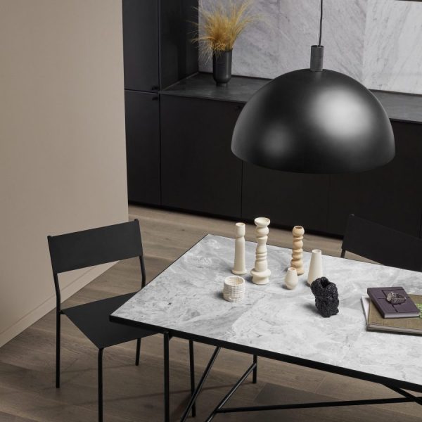 Et minimalistisk spiseområde med et sort marmorbord med unikke træskulpturer, omgivet af mørke stole, under en stor kuppelformet designpendul.