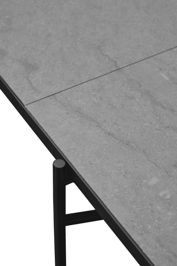 Nærbillede af et hjørne af en grå stenbordplade med synlig marmorering, designet af TomorrowsDesign, monteret på et sort metalbeslag, der er fastgjort til en sort overflade nedenunder.