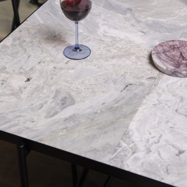 Et nærbillede af et marmorbord med et halvt glas rødvin og et rundt, pink-tonet designobjekt, muligvis en coaster eller en lille tallerken, på overfladen i indendørs omgivelser.
