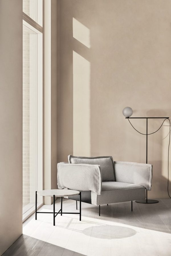 Minimalistisk interiør med en moderne grå sofa, et lille sort bord og en unik gulvlampe ved siden af et stort vindue, der kaster bløde skygger på den neutrale væg.