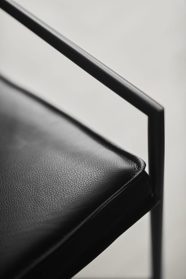 Nærbillede af en sort læderstol med fokus på dens teksturerede polstring og slanke metalstel, der viser en monokrom palet og minimalistisk TomorrowsDesign.