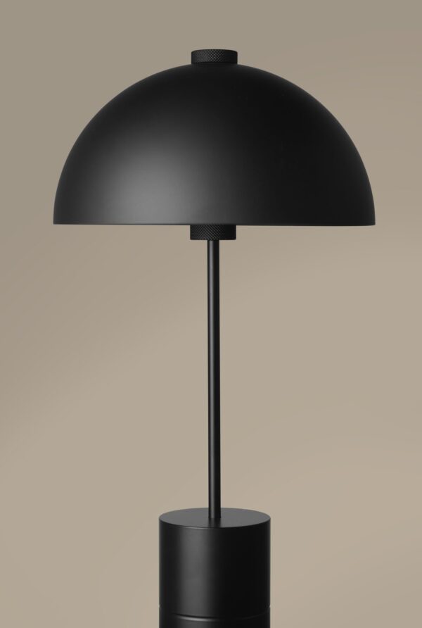En moderne sort skrivebordslampe med en stor kuppelformet skærm og en cylindrisk base, sat mod en neutral beige baggrund fra TomorrowsDesign.