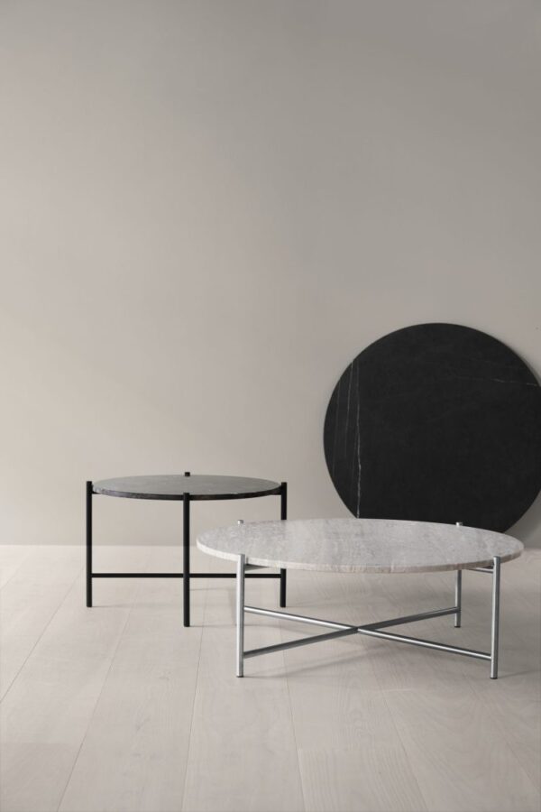 Et minimalistisk værelse med to moderne sofaborde med sorte stel, et med en rund marmorplade, og et andet mindre med en cirkulær sort plade, mod en beige væg og lyst trægulv. Denne opsætning inkluderer stykker fra TomorrowsDesign, der fremhæver deres unikke interiør-æstetik.