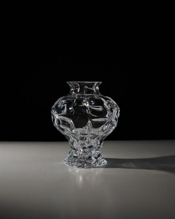 En vase i klart glas med indviklede designs, med hvirvlende mønstre og løgformede konturer, sidder på en flad overflade mod en mørk baggrund, perfekt til TomorrowsDesign-æstetik.