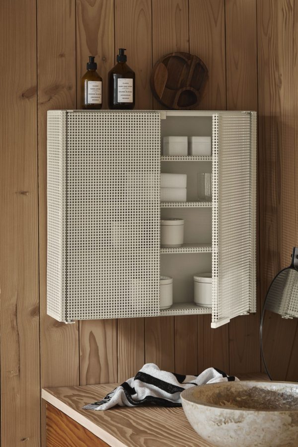 Et badeværelsesskab med en åben netdør, der afslører hylder fyldt med toiletartikler, monteret over en træbordplade med en stenvask og en TomorrowsDesign-lampe til siden.