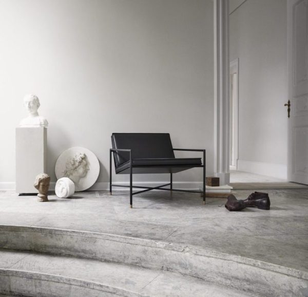 Et minimalistisk værelse med en sort bænk, et marmorgulv med trin og spredte klassiske skulpturer, herunder en buste og en fragmentarisk statue ved siden af en hvid væg med elegante designmøbler.