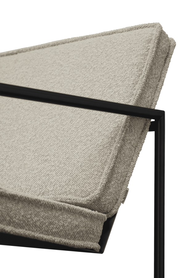 Nærbillede af en beige polstret bænkpude hvilende på en slank sort metalramme, der viser minimalistisk design, isoleret på en hvid baggrund.