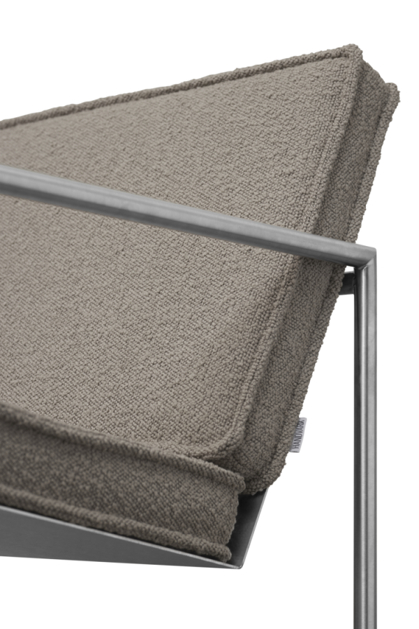 Nærbillede af en tekstureret beige pude på en moderne stol med metalstel med fokus på den detaljerede stofvævning og det elegante designmøbler-armlæn.
