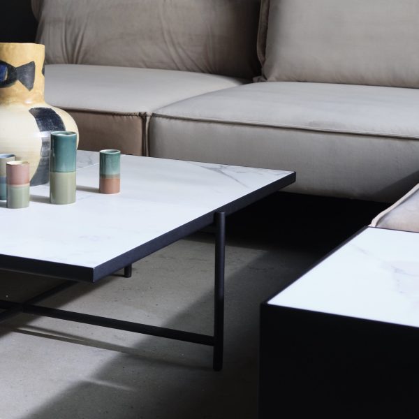 En moderne stue med en lys beige sofa og et HANDVÄRK MØBLER - Sofabord 90 med en lille samling farverige stearinlys og en stor dekorativ vase.