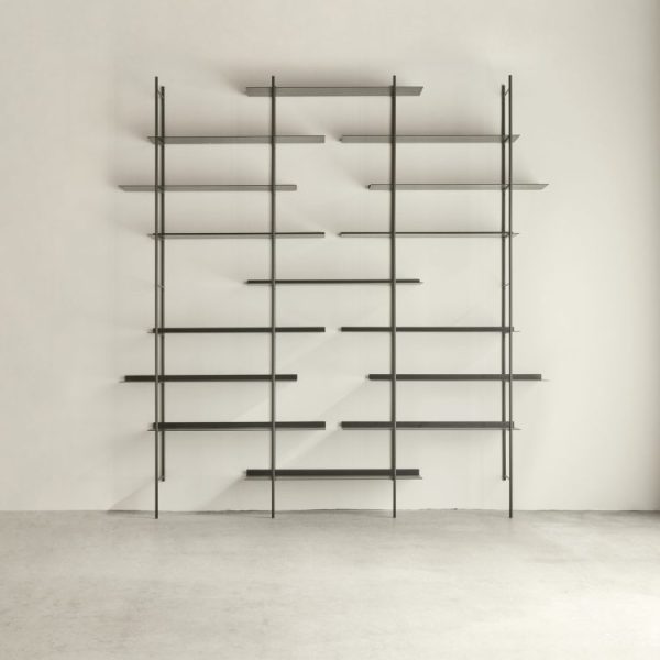 En minimalistisk metalreol med flere vandrette hylder mod en almindelig hvid væg i et tomt rum med et lysegråt gulv har TomorrowsDesign.