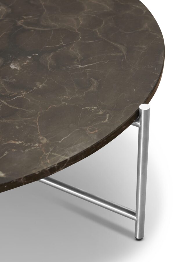 Nærbillede af et moderne sidebord med en rund, mørk marmorplade og slanke, sølvmetalben på hvid baggrund. Bordet viser naturstensmønstre og et minimalistisk interiørdesign.