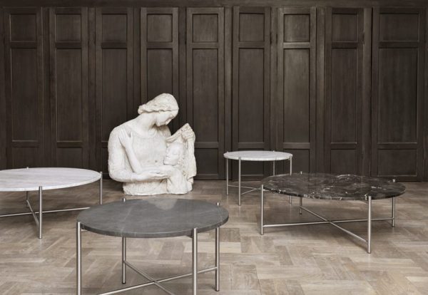 En marmorskulptur af en siddende kvinde, der læser for et barn i et rum med mørke træpanelvægge og fire minimalistiske designmøbler sofaborde med forskellige designs på et trægulv.