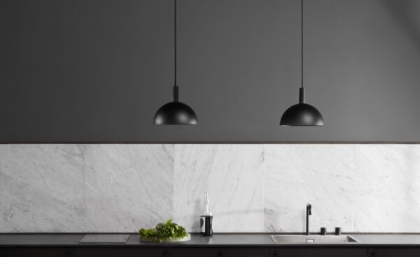 To sorte pendellamper hænger over en moderne køkkenbord med en hvid marmorbagplade og mørke skabe, der viser et TomorrowsDesign minimalistisk interiør.