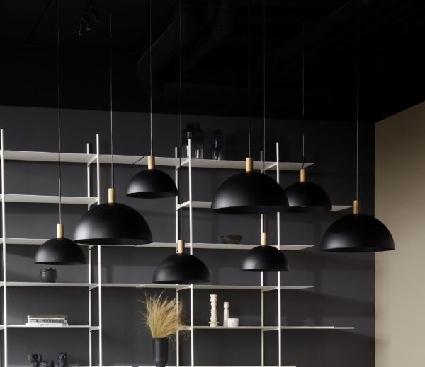 Moderne interiør med minimalistiske matsorte pendellamper, der hænger over en hvid reol med forskellige dekorative genstande, mod en mørkegrå baggrund.