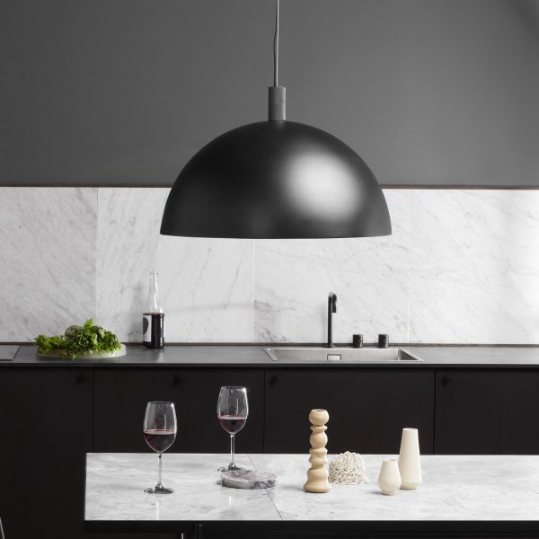Et moderne køkken med en stor sort pendel over en marmorø. Øen byder på to glas rødvin, dekorative vaser og en baggrund af slanke marmorvægge med sorte TomorrowsDesign-skabe.