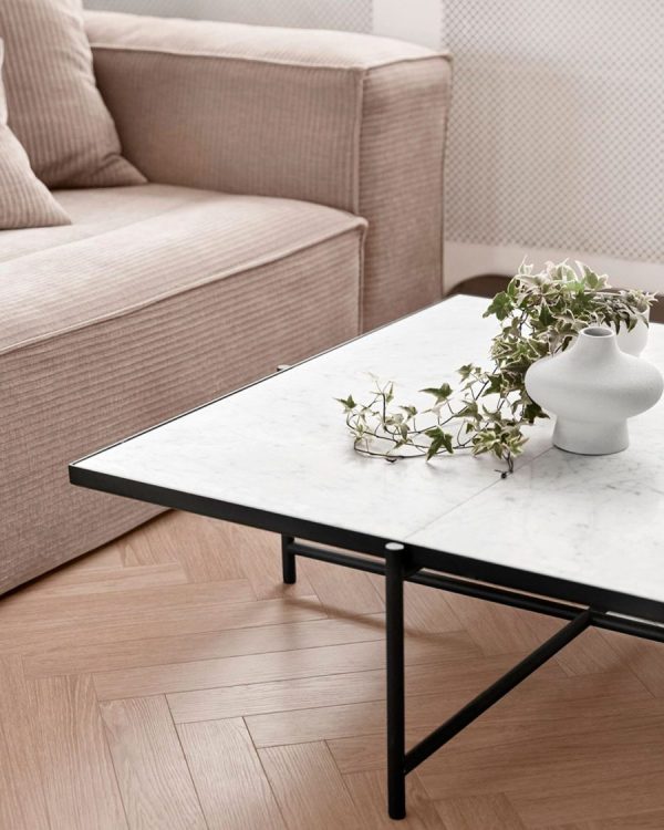 En minimalistisk stue med en beige sofa og et rektangulært sofabord i marmor med sort stel. På bordet står en lille, hvid vase med slæbende grønne planter. Dette rum er indbegrebet af moderne design.