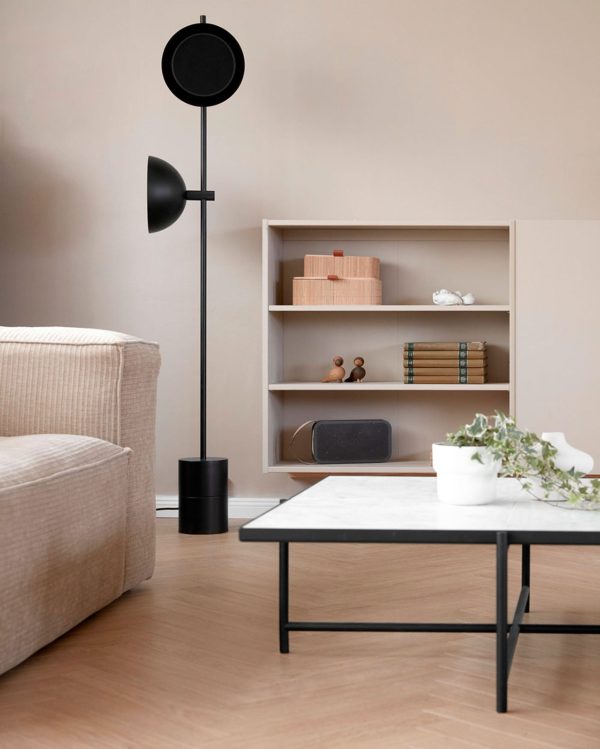 Et moderne stuehjørne med en beige sofa, en sort gulvlampe, et lavt sort sofabord og en bogreol i træ med et par bøger og dekorative TomorrowsDesign-ting. Lyse beige vægge komplementerer de neutrale toner.