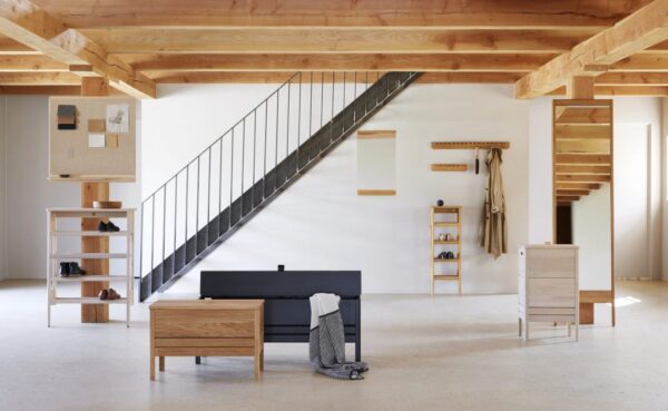Et minimalistisk interiør med et åbent rum med synlige træbjælker, en enkel trætrappe med sort metalgelænder, FORM & REFINE - Echo Knagerække 88 møbler og en velorganiseret reol.