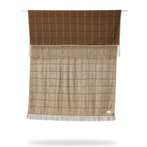 A FORM & REFINE - Aymara Plaid New Square 130x190 tæppe med frynser, hængende lodret mod en hvid baggrund.