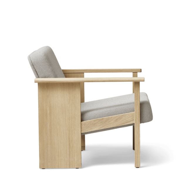 A FORM & REFINE - Block Lænestol Grain lænestol med lysegrå hynder, udstillet mod en ensfarvet grøn baggrund. designet byder på rene linjer og en minimalistisk stil.