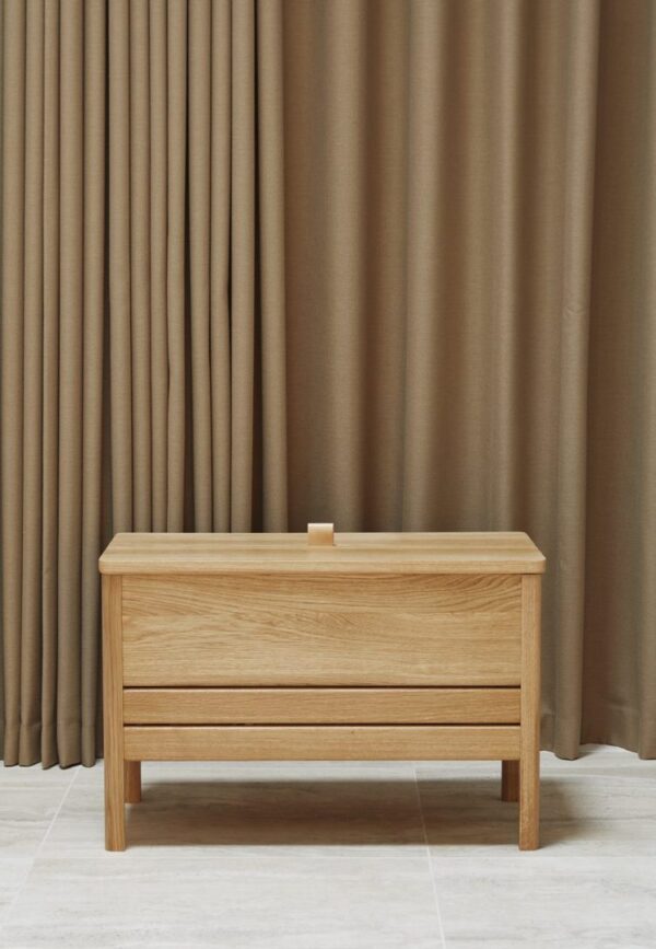 A FORM & REFINE - En Line Slagbænk 68 placeret foran et gulv til loft brunt gardin i et rum med klinkegulv. der er en lille, firkantet, beige beholder på bænken.