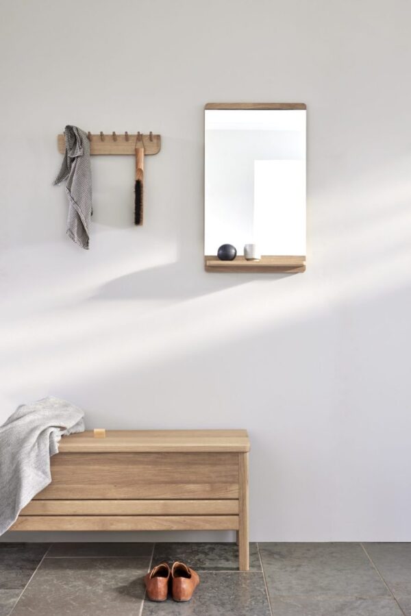 En minimalistisk entré med en træbænk, FORM & REFINE - Rim Vægspejl på væggen og en enkel knagerække med et gråt tørklæde og en børste. Et par lædersko er placeret pænt på gulvet.
