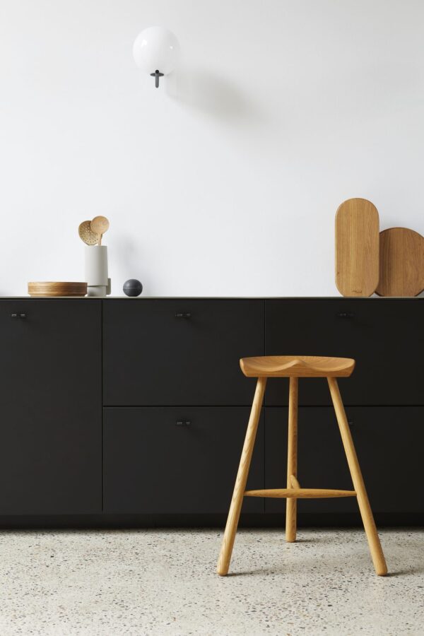 Et minimalistisk moderne køkkeninteriør med en sort FORM & REFINE - Shoemaker Barstol No. 68 med terrazzogulve og en hvid væg med en enkelt kugleformet lysarmatur i forgrunden.