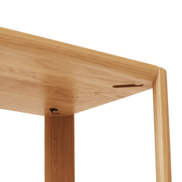 Nærbillede af et lyst træhjørne af et FORM & REFINE - Leaf Reol 1x3 bord, der viser detaljeret snedkerarbejde og et mærkelogo ætset på siden.