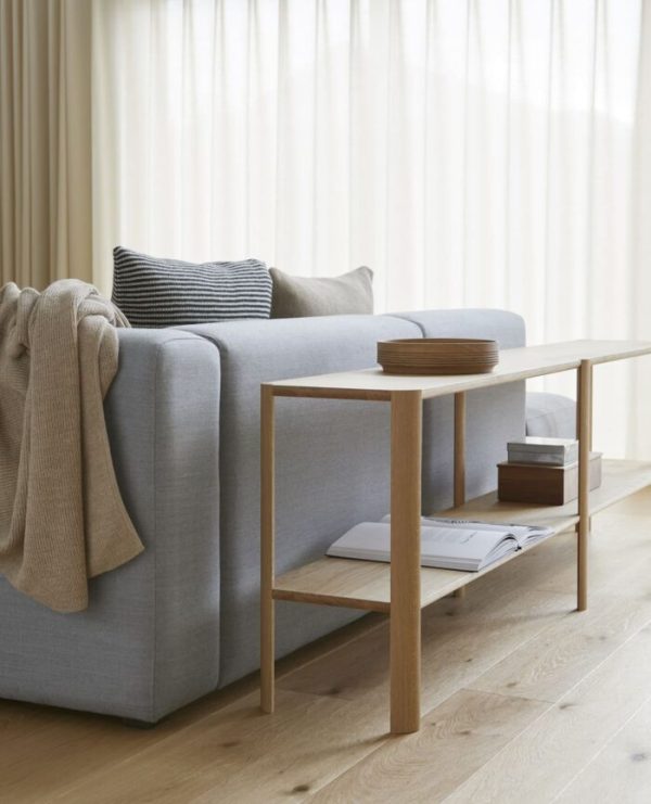 A FORM & REFINE - Leaf Reol 2x2 stue med en lysegrå sofa med solbrun og stribet pude ved siden af et sofabord i træ med bøger og små trækasser, alt sammen sat mod rene gardinvinduer og et trægulv.