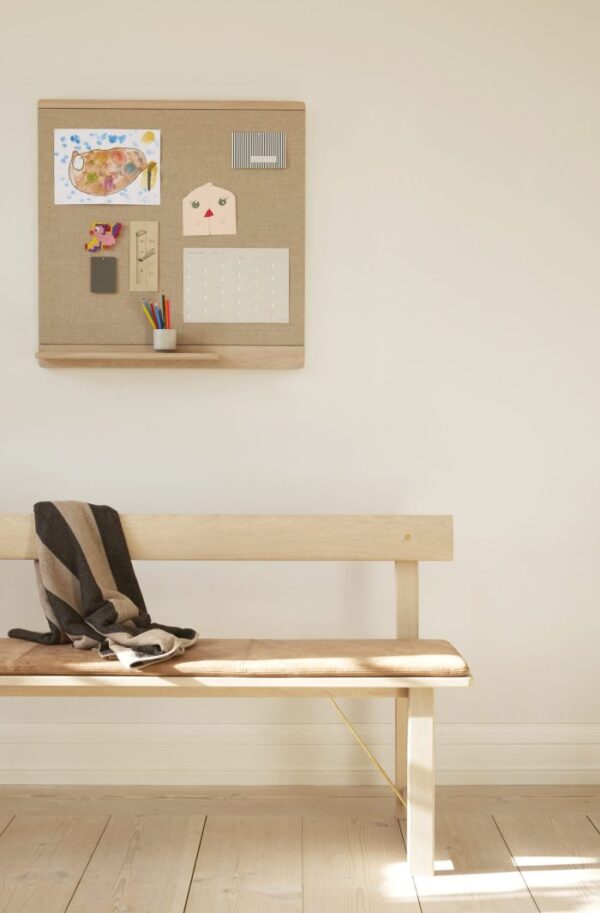 En minimalistisk entré med en bænk med FORM & REFINE - Aymara Plaid Ribbon 190x130 og sko placeret på gulvet. Over bænken hænger en korktavle med et verdenskort, en kalender og nogle farveblyanter.